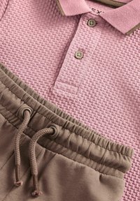 Polo shirt testurizzato rosa chiaro con colletto marrone e bottoni sopra pantaloni della tuta beige con fascetta. Tessuto morbido e vestibilità rilassata.
