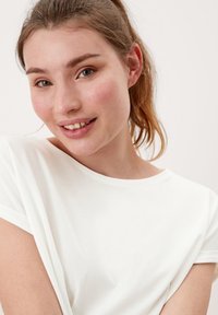 Witte t-shirt met een ronde halslijn en korte opgerolde mouwen. Zacht katoenen materiaal, lichtjes gedrapeerde pasvorm, gladde textuur, minimale details.