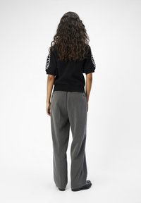 Top negro de punto con mangas cortas y texturizadas; pantalones grises de pierna ancha con un patrón sutil; calzado oscuro y liso.