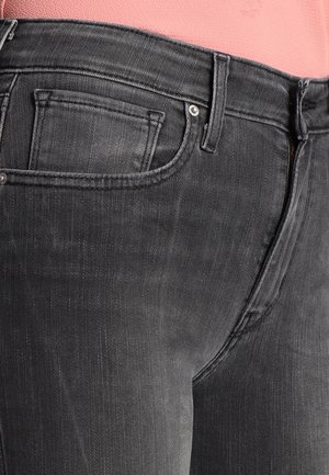 Jean en denim noir porté avec un haut rose, montrant la poche avant et les passants de ceinture en vue rapprochée.