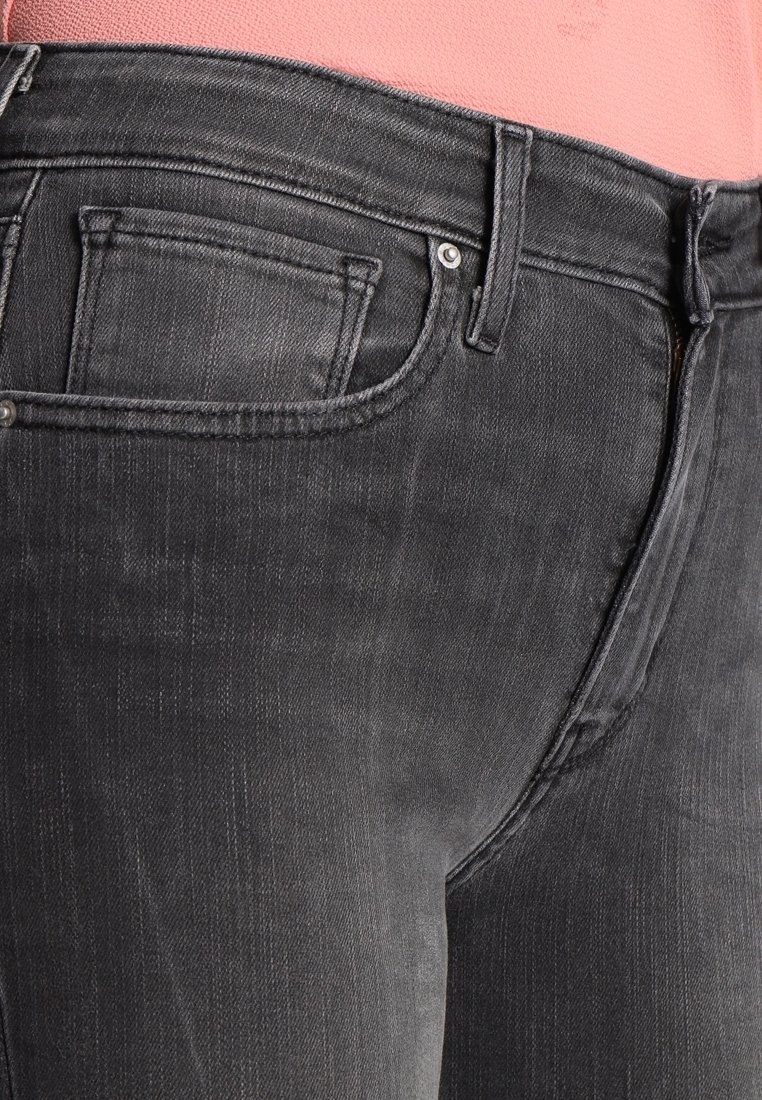 Jean en denim noir porté avec un haut rose, montrant la poche avant et les passants de ceinture en vue rapprochée.