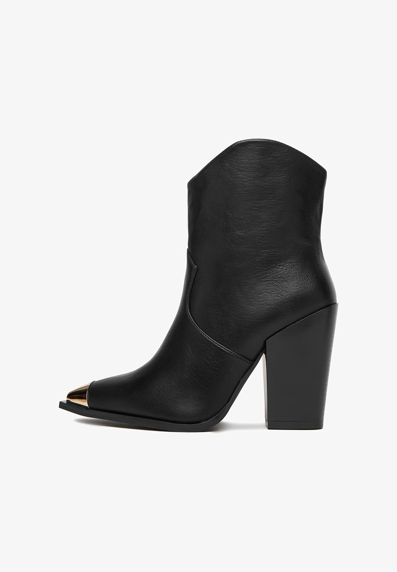 Czarny skórzany botek za kostkę z wysokim słupkowym obcasem i spiczastym noskiem, z złotym metalowym akcentem na czubku. Gładka tekstura.