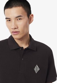 Čierne polo tričko z textúrovaného materiálu, s golierom, dvoma gombíkmi a bielym vyšívaným diamantovým logom na hrudi.