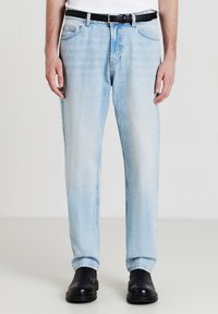 Jean en denim bleu clair avec une coupe droite, présentant un design classique à cinq poches, un léger décoloration et une ceinture en cuir noir.