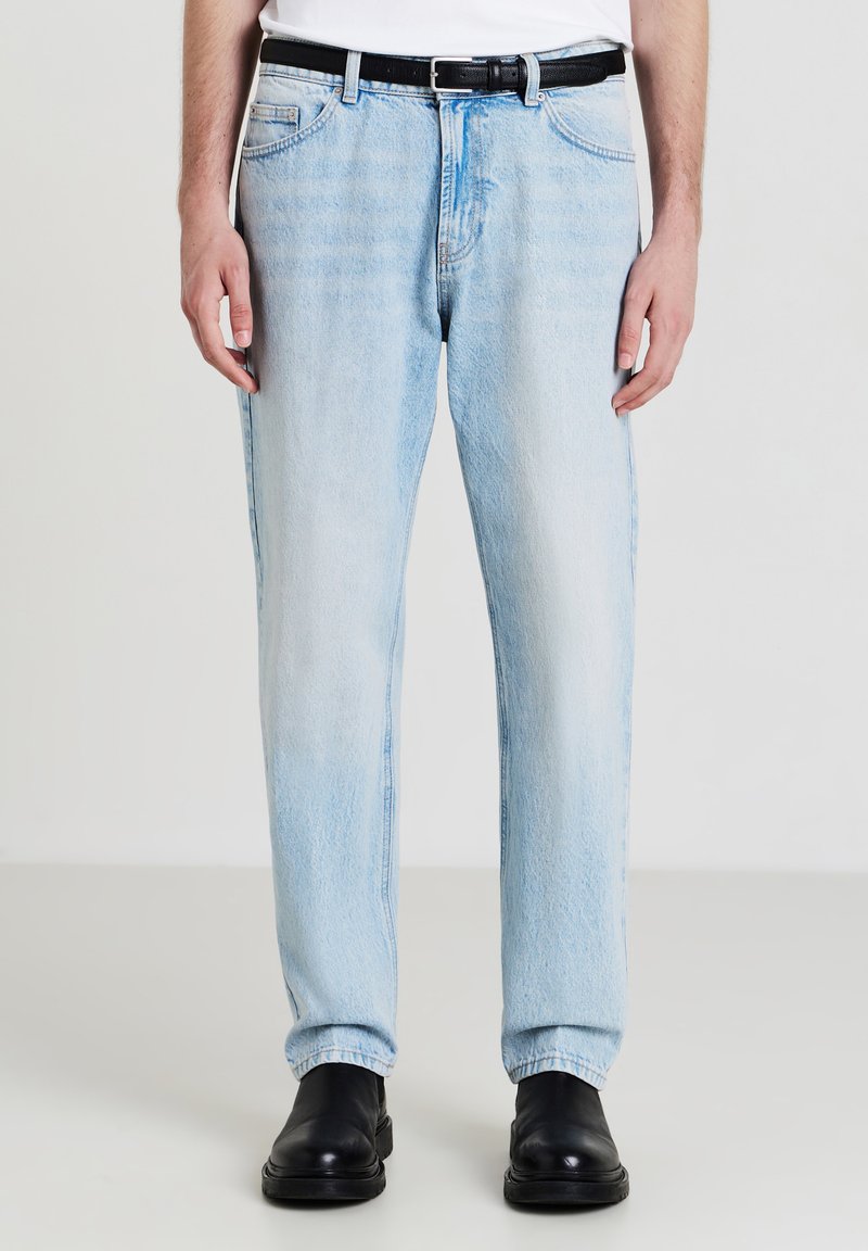 Jean en denim bleu clair avec une coupe droite, présentant un design classique à cinq poches, un léger décoloration et une ceinture en cuir noir.