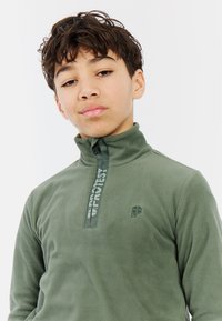 Pullover in pile verde con colletto alto e zip a metà. Presenta un logo sul petto e una striscia testurizzata con la scritta "PROTEST".