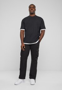 Sort kortærmet t-shirt med hvid kant, parret med sorte cargo-bukser med lommer og hvide sneakers. Enkelt og funktionelt design.