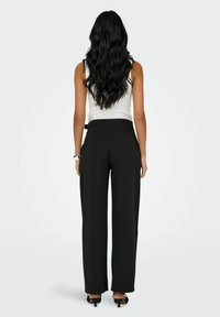 Černé kalhoty s širokými nohavicemi a vysokým pasem s nenápadnými bočními kapsami, doplněné o bílé přiléhavé tílko, pohled zezadu.