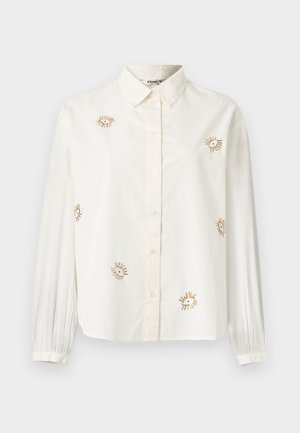 Λευκό πουκάμισο με κουμπιά κατασκευασμένο από βαμβάκι, με χρυσή κεντημένη ηλιαχτίδα και μακριά μανίκια με πιετέ μανσέτες. Κλασικό σχέδιο για το γιακά.