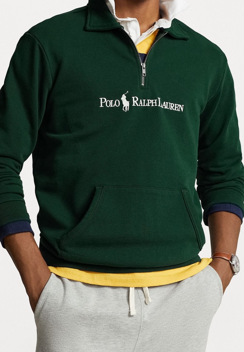 Felpa verde con zip a quarto e colletto alto, dotata di tasca frontale. Presenta il logo bianco "Polo Ralph Lauren" e design sovrapposti gialli e blu navy sottostanti.