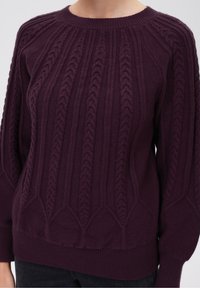 Strickpullover in tiefem Lila mit erhabenen Zopfmustern, Ribkragen und -bündchen sowie einem lässigen Schnitt mit strukturierten Details.