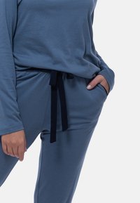 Jasnoniebieski zestaw wypoczynkowy, składający się z długiego rękawa i spodni na sznurku. Materiał wydaje się miękki, z luźnym krojem i kieszeniami.