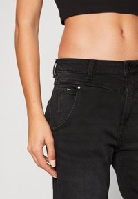 Svarta högmidjade jeans i denim med en figurnära design, subtil slitage och en liten silverlogga på framfickan.