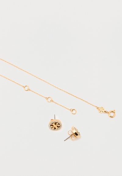 Zlatna ogrlica s delikatnim lancem i kopčom, u paru s naušnicama na dugme koje imaju dizajn s leopard uzorkom i kristalnim akcentima.