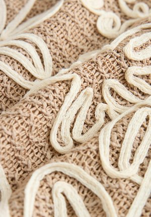 Gestickter Stoff in Beige mit cremefarbener Fadengestaltung, die komplexe Wirbel bildet und eine strukturierte, gewebte Oberfläche zeigt.