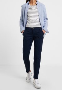 Modrá lněná košile na knoflíky přes pruhované tričko, spárovaná s úzkými kalhotami v námořnické barvě a bílými teniskami.