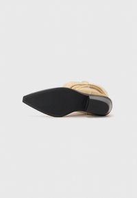 Chaussure à talons aiguilles en daim beige avec un bout pointu, dotée d'une semelle en caoutchouc noir texturé et d'un talon élancé.