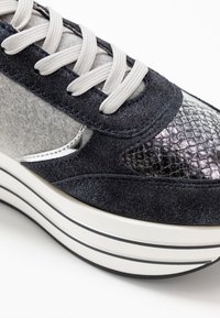 Suede sneaker in dark navy with silver accents and a textured snake-skin toe cap. Thick white sole with black stripes and gray laces.