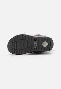 Suela de zapato negra de goma con patrón texturizado y ranuras flexibles. Presenta un logo redondo y una marca en el talón para mayor agarre y estabilidad.