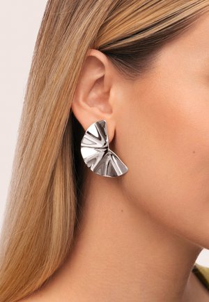 Zilveren metalen oorbellen met een waaiervormig ontwerp, gekenmerkt door textuurrijke, reflecterende oppervlakken en duidelijke hoekige groeven.