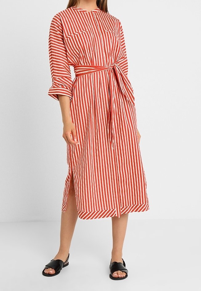 Rød- og hvidstribet kjole med taljebånd, lange ærmer og sidelommer. Fremstillet i letvægtsstof, med rund halsudskæring og manchetter.