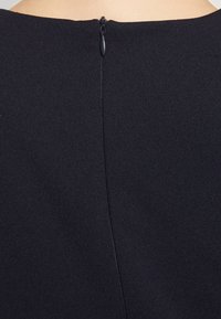 Ναυτικό φόρεμα με λεία υφή, διαθέτοντας διακριτικό φερμουάρ στο πίσω μέρος και καθαρή, στρογγυλή λαιμόκοψη. Το υλικό φαίνεται ελαφρύ και ροδαλό.