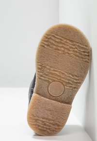 Soletta nera di scarpa con una superficie testurizzata, caratterizzata da motivi ondulati e un dettaglio di marchio circolare. Materiale in gomma marrone chiaro.