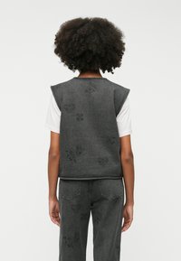 Jeansvest i mørkegrått med tekstilapplikasjoner som viser ulike blomster- og hjerte-design. Uten ermer med avrundet kant og enkle sømdetaljer.