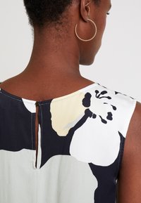 Abito senza maniche con stampa floreale nei colori nero, crema e verde pallido. Chiusura con bottoni sul retro e design a occhiello sul collo.
