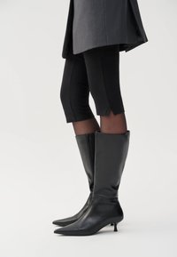 Black knee-high boots made of smooth leather with pointed toes and a small kitten heel. The design includes a side zipper for fastening.