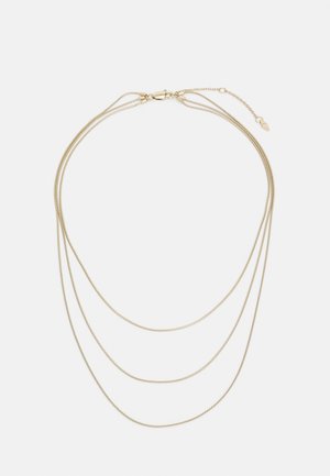 Collier délicat ton or avec trois chaînes fines superposées et un fermoir mousqueton avec longueur réglable sur fond blanc.