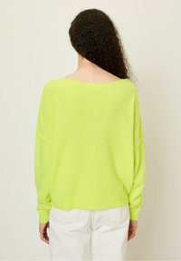 Neon groene, oversized trui met een wijde halslijn, gevallen schouders en geribde manchetten. Zachte, gestructureerde stof, gecombineerd met witte broek.