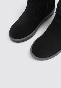Botines de ante negro con una superficie suave y acentos texturizados, que cuentan con una suela de goma y detalles cosidos en los bordes.