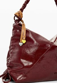 Bolso de cuero burdeos con un asa trenzada en color beige, adornado con charms en forma de corazón en plata y amarillo, textura suave y detalles cosidos.