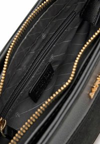 Interno della borsa in pelle nera che mostra una tasca con zip, foderata in tessuto nero con motivi sottili e dettagli in oro.