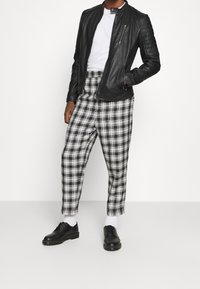 Svart läderjacka med dragkedja och vadderade axlar, kombinerad med svart-vitt rutigt byxor och svarta skor. Vit t-shirt under.