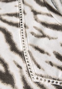 White fabric with black and grey animal print pattern, featuring a decorative trim with small holes along the seam for added detail.