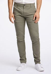 Slim-Fit, olivgrüne Chinos aus Baumwollmischgewebe, mit Knopfverschluss, Seitentaschen und passender Steppnaht zu weißen Sneakers.