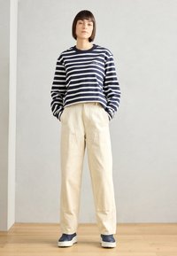 Marineblå og hvitstripete langermet crop topp, beige vide bukser og marineblå joggesko med strukturert såle, satt mot en nøytral bakgrunn.
