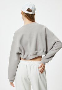 Felpa grigia accorciata con colletto rotondo e spalle cadenti. Abbinata a pantaloni tuta bianchi con vita elastica, caratterizzati da una vestibilità casual.