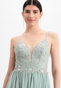 Minzgrünes Kleid mit filigraner silberner Stickerei und Perlen, ausgestattet mit einem tiefen V-Ausschnitt und dünnen Trägern, fließendem Rockdesign.