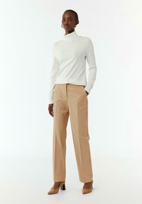 Pullover bianco a collo alto abbinato a pantaloni beige su misura e scarpe con tacco alti color nocciola, con una texture liscia e linee pulite.