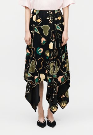 Zwarte asymmetrische rok met kleurrijke bloem- en hartmotieven, gedragen met zwarte pumps met puntige neus en een lichtroze top.