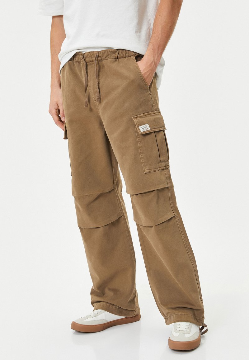Khaki cargobroeken met een elastische tailleband, twee zijzakken en twee grote dijzakken. Gemaakt van duurzaam katoen.