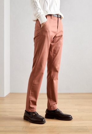 Rozsdabarna, slim-fit nadrág oldalzsebbel és sima textúrával, sötét mokaszinokkal arany részlettel párosítva.