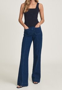 Mörkblå utsvängda jeans med fram- och bakfickor, som har blå sömmar och en ren fåll, i kombination med en åtsittande svart linne.