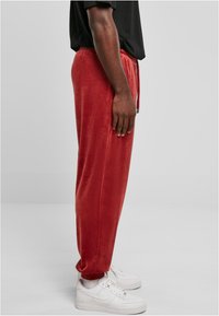 Red, soft joggers made of plush material, featuring an elastic waistband with drawstring, ribbed cuffs, and paired with white sneakers.