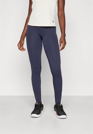 Leggings a costine di colore blu navy con vestibilità slim, abbinati a una maglietta chiara a maniche corte. Scarpe da ginnastica nere completano l'outfit.