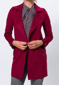 Bordeaux neplederen jas met een geknipt kraag, voorzakken met rits en lange mouwen, gelaagd over een gebloemde blouse.