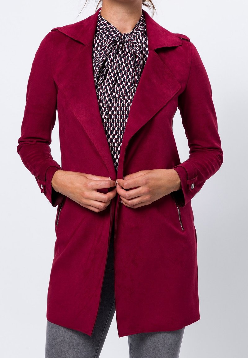 Bordeaux neplederen jas met een geknipt kraag, voorzakken met rits en lange mouwen, gelaagd over een gebloemde blouse.